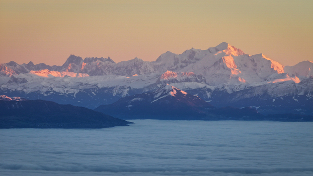 Aerial view of the snow covered peaks of the Mont Blanc massif glowing in the golden light of sunset above a thick layer of clouds Chamonix Auvergne Rhone Alpes France. Aerial view of the snow covered peaks of the Mont Blanc massif glowing in the golden light of sunset above a thick layer of clouds Chamonix Auvergne Rhone Alpes France.