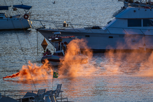 Rio de Janeiro Brazil 18 June 2026 View of naval training exercise with a small boat deploying orange smoke in the water surrounded by yachts at sunset.