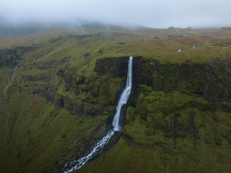 Aerial view of a cascading waterfall cutting through the rugged moss covered cliffs under a heavy grey sky Snæfellsnes Eyja og Miklaholtshreppur Iceland. Aerial view of a cascading waterfall cutting through the rugged moss covered cliffs under a heavy grey sky Snæfellsnes Eyja og Miklaholtshreppur Iceland.