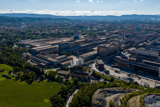 Aerial view of the Acciai Speciali Terni S.p.A. steel plant complex with large industrial warehouses chimneys and surrounding green landscape in Terni Umbria Italy.