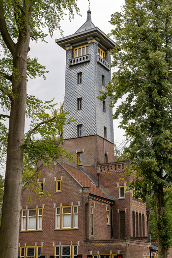 View of the historic De Brandtoren tower with its distinctive tiled facade and brick architecture surrounded by lush green trees in Esbeek Noord Brabant Netherlands.
