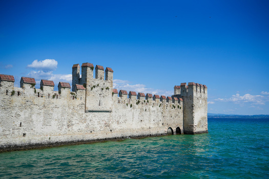 View of the historic Scaligero Castle walls and towers rising from the turquoise waters of Lake Garda under a clear blue sky in Sirmione Lombardy Italy.