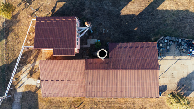 Aerial view of an industrial facility with metal roofs a central chimney and surrounding dry grassy terrain in Sremska Mitrovica Vojvodina Serbia. Aerial view of an industrial facility with metal roofs a central chimney and surrounding dry grassy terrain in Sremska Mitrovica Vojvodina Serbia.