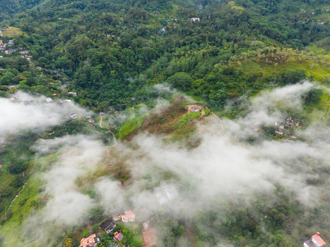 Aerial view of lush green hills and dense tropical forest partially covered by low lying mist and clouds with scattered houses on the slopes in Kandy Central Province Sri Lanka. Aerial view of lush green hills and dense tropical forest partially covered by low lying mist and clouds with scattered houses on the slopes in Kandy Central Province Sri Lanka.