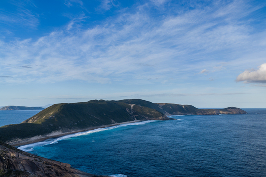 Aerial view of Salmon Holes with turquoise ocean waves crashing against rocky cliffs and coastal hills under a blue sky in Torndirrup Western Australia Australia.