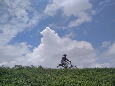 Kushtia Khulna Division Bangladesh 27 April 2020 View of a man riding a bicycle along a grassy embankment under a bright blue sky with large white clouds. Kushtia Khulna Division Bangladesh 27 April 2020 View of a man riding a bicycle along a grassy embankment under a bright blue sky with large white clouds.