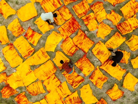 Narayanganj Bangladesh 30 March 2026 Aerial view of vibrant yellow fabrics patterned with fiery red drying under the sun as workers tend to the textile spread.