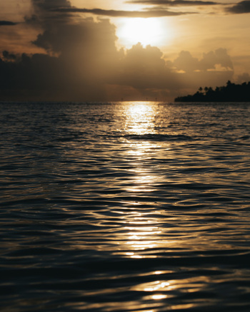 View of golden sunlight reflecting on the tranquil waters as clouds gather over a distant island creating a serene coastal scene Lata Solomon Islands.