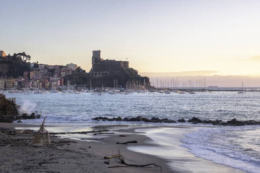 View of the historic Castello di Lerici overlooking the harbor filled with sailboats and colorful coastal houses from the sandy Venere Azzurra beach at sunset Lerici Liguria Italy.
