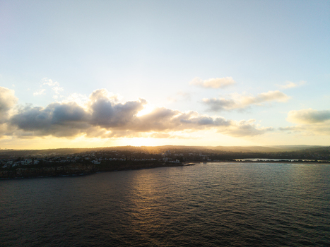 Aerial view of the coastline at Dee Why during sunset with golden light reflecting on the ocean and clouds over the residential clifftops in Dee Why New South Wales Australia. Aerial view of the coastline at Dee Why during sunset with golden light reflecting on the ocean and clouds over the residential clifftops in Dee Why New South Wales Australia.