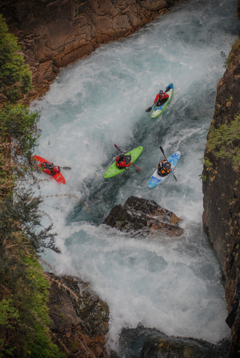 View of kayakers navigating the white water rapids of Rio Manso through a narrow rocky canyon with lush vegetation in San Carlos de Bariloche Rio Negro Argentina. View of kayakers navigating the white water rapids of Rio Manso through a narrow rocky canyon with lush vegetation in San Carlos de Bariloche Rio Negro Argentina.