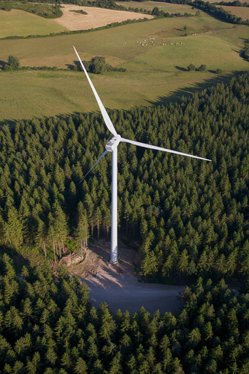Aerial view of a solitary wind turbine rises majestically amidst a dense forest contrasting against the open fields beyond Salles Curan Occitanie France. Aerial view of a solitary wind turbine rises majestically amidst a dense forest contrasting against the open fields beyond Salles Curan Occitanie France.