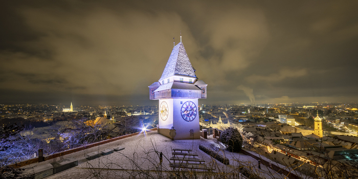 View of the iconic clock tower bathed in a soft glow overlooking a snow dusted cityscape under a moody sky Graz Styria Austria. View of the iconic clock tower bathed in a soft glow overlooking a snow dusted cityscape under a moody sky Graz Styria Austria.