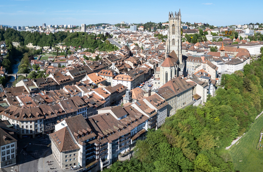 Aerial view of St Nicolas Cathedral surrounded by historic red tiled rooftops and lush greenery in Fribourg Fribourg Switzerland. Aerial view of St Nicolas Cathedral surrounded by historic red tiled rooftops and lush greenery in Fribourg Fribourg Switzerland.