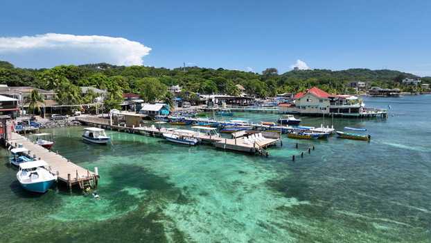 Aerial view of West End featuring wooden docks colorful boats and clear turquoise water along the lush coastline in West End Bay Islands Department Honduras.