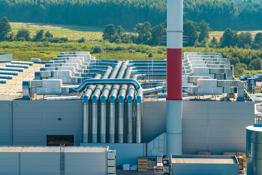 Aerial view of an advanced motorboat production facility featuring extensive rooftop ventilation systems metallic pipes and a tall red and white chimney surrounded by lush green forest in Poland.