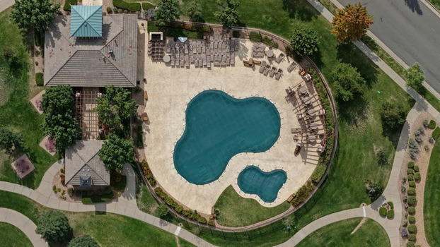 Aerial view of a community swimming pool with green covers lounge chairs and a pergola surrounded by landscaped grass and pathways in Golden Colorado United States.