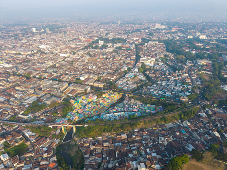 Aerial view of the vibrant Jodipan Colorful Village with its brightly painted houses situated along the river and railway bridge in the dense urban landscape of Malang East Java Indonesia.