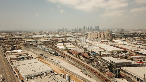 Aerial view of the Los Angeles skyline rising above industrial warehouses rail tracks and urban infrastructure in Los Angeles California United States. Aerial view of the Los Angeles skyline rising above industrial warehouses rail tracks and urban infrastructure in Los Angeles California United States.