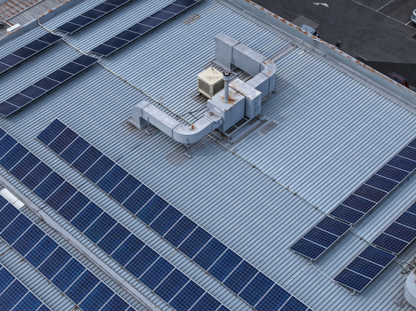Aerial view of solar panels installed on a corrugated metal industrial roof with HVAC units and ventilation pipes in Melbourne VIC Australia.