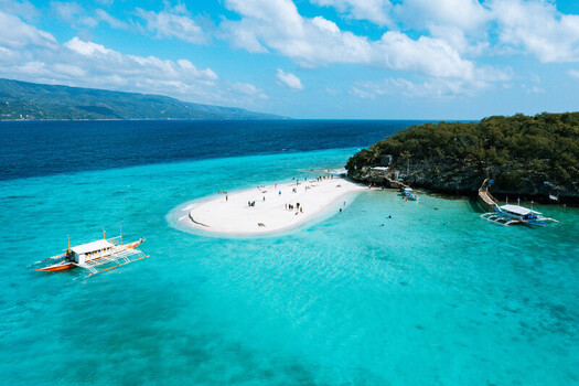 Aerial view of the Sumilon Island sandbar surrounded by turquoise waters outrigger boats and people on the beach in Oslob Cebu Philippines. Aerial view of the Sumilon Island sandbar surrounded by turquoise waters outrigger boats and people on the beach in Oslob Cebu Philippines.