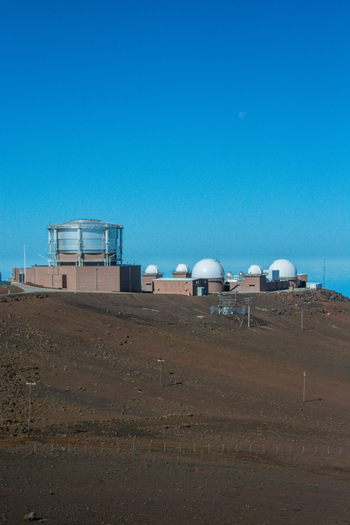 View of the Haleakala Observatory with its white telescope domes set against a clear blue sky and the volcanic landscape of Maui County Hawaii United States.