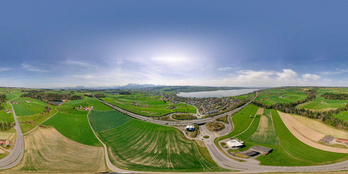 Aerial view of the Schlachtkapelle in a 360 degree panorama featuring lush green fields winding highways and Lake Sempach under a clear blue sky Sempach Luzern Switzerland.