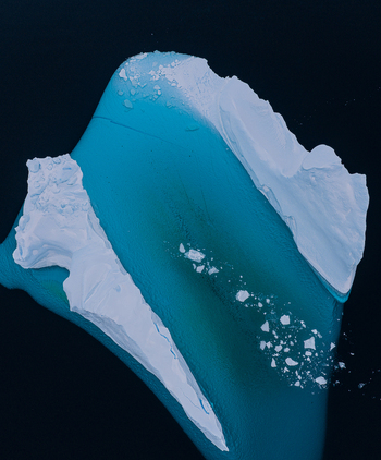 Aerial view of a large iceberg with turquoise ice and white snow floating in dark arctic waters near Tasiilaq Sermersooq Municipality Greenland. Aerial view of a large iceberg with turquoise ice and white snow floating in dark arctic waters near Tasiilaq Sermersooq Municipality Greenland.