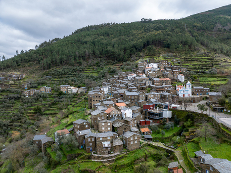 Aerial view of stone houses cascading down the hillside towards the church with blue trim under a grey sky Piódão Arganil Portugal. Aerial view of stone houses cascading down the hillside towards the church with blue trim under a grey sky Piódão Arganil Portugal.