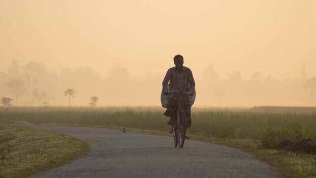 View of a man riding a bicycle on a misty road in Bogura Bangladesh.