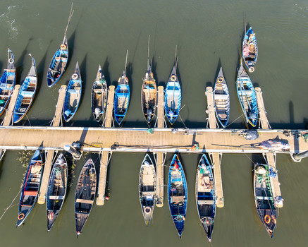 Aerial view of fishing boats line the pier their vibrant hulls a stark contrast to the dark waters surrounding Porta de Abrigo da Torreira Aveiro Portugal.
