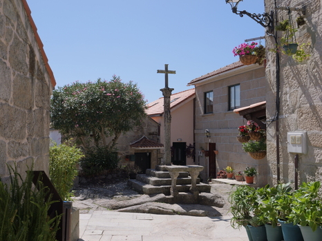 View of the historic stone cross in the village of Combarro featuring traditional granite architecture hanging flower baskets and lush greenery in Combarro Pontevedra Spain.