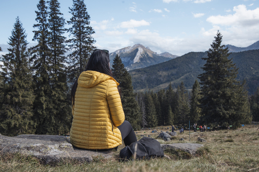 View of a woman in a yellow jacket sitting on a rock and looking at a mountain landscape with pine trees in Poland. View of a woman in a yellow jacket sitting on a rock and looking at a mountain landscape with pine trees in Poland.