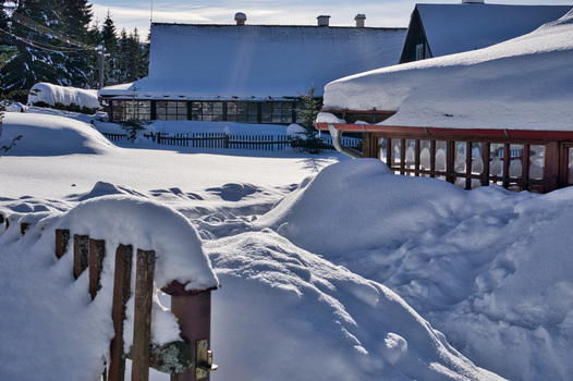 View of a snow laden landscape where buildings are blanketed in white and a rustic fence peeks through the drifts creating a serene winter scene Donovaly Banskobystricky kraj Slovakia. View of a snow laden landscape where buildings are blanketed in white and a rustic fence peeks through the drifts creating a serene winter scene Donovaly Banskobystricky kraj Slovakia.