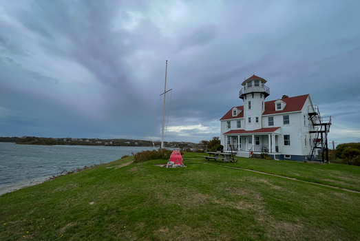View of the historic Block Island North Lighthouse with white exterior and red roof on a grassy coastal bluff overlooking the ocean in New Shoreham Rhode Island United States.