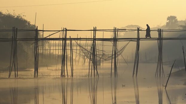 View of a person walking on a bamboo bridge at sunrise Bangladesh.