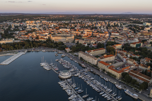 Aerial view of the historic Pula Arena surrounded by the city skyline marina with docked boats and coastal landscape in Pula Istarska zupanija Croatia. Aerial view of the historic Pula Arena surrounded by the city skyline marina with docked boats and coastal landscape in Pula Istarska zupanija Croatia.