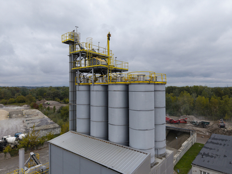 Aerial view of the asphalt plant with tall grey storage silos and yellow metal platforms surrounded by gravel piles and industrial equipment in Krakow Lesser Poland Voivodeship Poland.