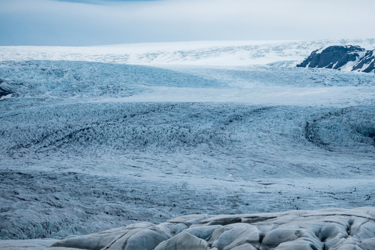 View of Vatnajokull glacier with deep crevasses and icy textures under a cloudy sky in Iceland.