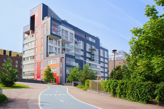 View of a modern apartment building with a colorful facade and glass balconies situated next to a paved bicycle path surrounded by green trees in Helsinki Uusimaa Finland.