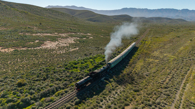 Aerial view of a vintage steam train billowing white smoke as it travels through the rugged semi arid landscape and rolling hills in Robertson Western Cape South Africa.