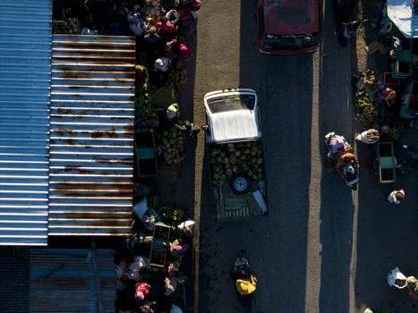 Aerial view of a white pickup truck carrying coconuts through a busy street market with people and stalls in Kemalang Central Java Indonesia.