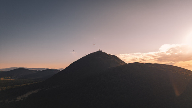 Aerial view of the Puy de Dome peak at sunset with paragliders soaring in the sky in Orcines Auvergne Rhone Alpes France. Aerial view of the Puy de Dome peak at sunset with paragliders soaring in the sky in Orcines Auvergne Rhone Alpes France.