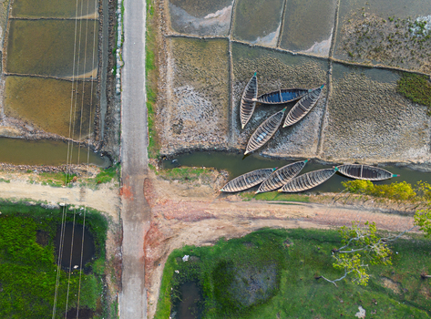 Aerial view of traditional wooden boats moored in a narrow canal beside salt pans and a rural road in Moheskhali Upazila Chittagong Division Bangladesh. Aerial view of traditional wooden boats moored in a narrow canal beside salt pans and a rural road in Moheskhali Upazila Chittagong Division Bangladesh.