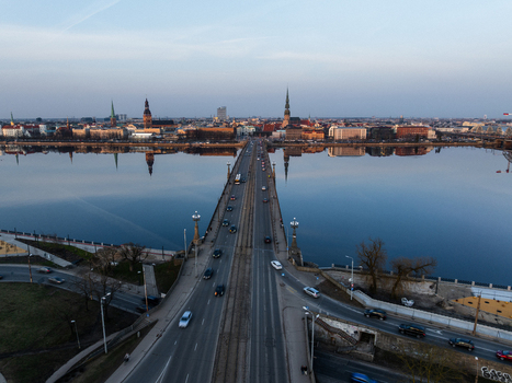 Aerial view of Akmens tilts crossing the Daugava River towards the historic Old Town of Riga at sunset with city skyline and calm water reflections Riga Latvia. Aerial view of Akmens tilts crossing the Daugava River towards the historic Old Town of Riga at sunset with city skyline and calm water reflections Riga Latvia.