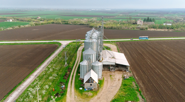 Aerial view of silver grain silos standing tall amidst the rich dark earth of cultivated fields under a soft overcast sky Sremska Mitrovica Vojvodina Serbia. Aerial view of silver grain silos standing tall amidst the rich dark earth of cultivated fields under a soft overcast sky Sremska Mitrovica Vojvodina Serbia.