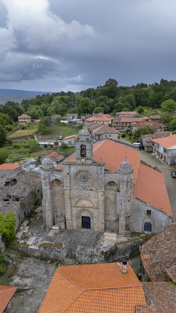 Aerial view of the historic Iglesia de Santa Marina de Augas Santas with its stone facade and red tiled roof surrounded by village houses and green hills in Augas Santas Ourense Spain. Aerial view of the historic Iglesia de Santa Marina de Augas Santas with its stone facade and red tiled roof surrounded by village houses and green hills in Augas Santas Ourense Spain.