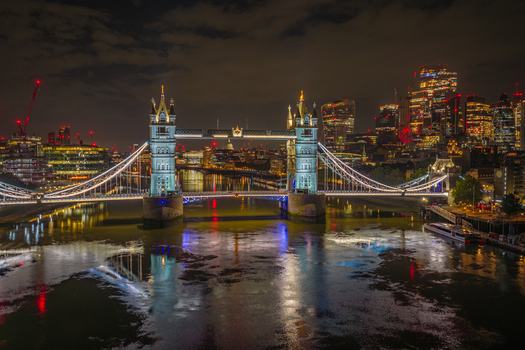 Aerial view of Tower Bridge illuminated at night with the River Thames reflecting the lights and the City of London skyline in the background London England United Kingdom.