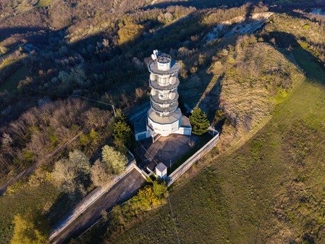 Aerial view of the Television Tower Tortona standing on a green hilltop surrounded by dense trees and rolling hills under soft sunlight Tortona Piedmont Italy.