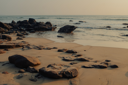View of scattered rocks adorn the sandy beach where the sea meets the shore under a soft golden light Chiplun Maharashtra India. View of scattered rocks adorn the sandy beach where the sea meets the shore under a soft golden light Chiplun Maharashtra India.